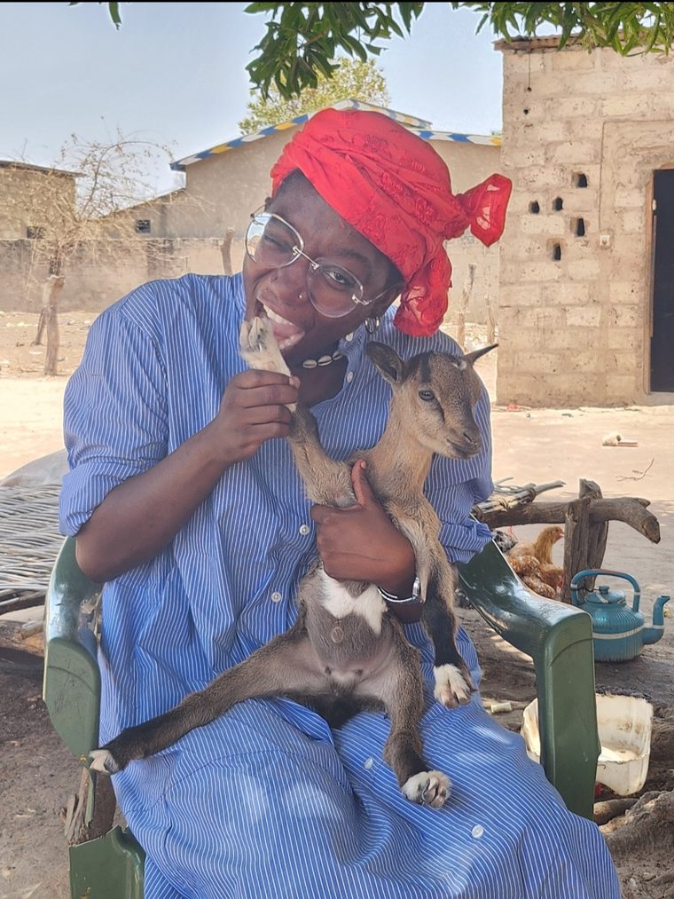 Bre Rogers smiling in a family compound in Senegal, holding a young goat
